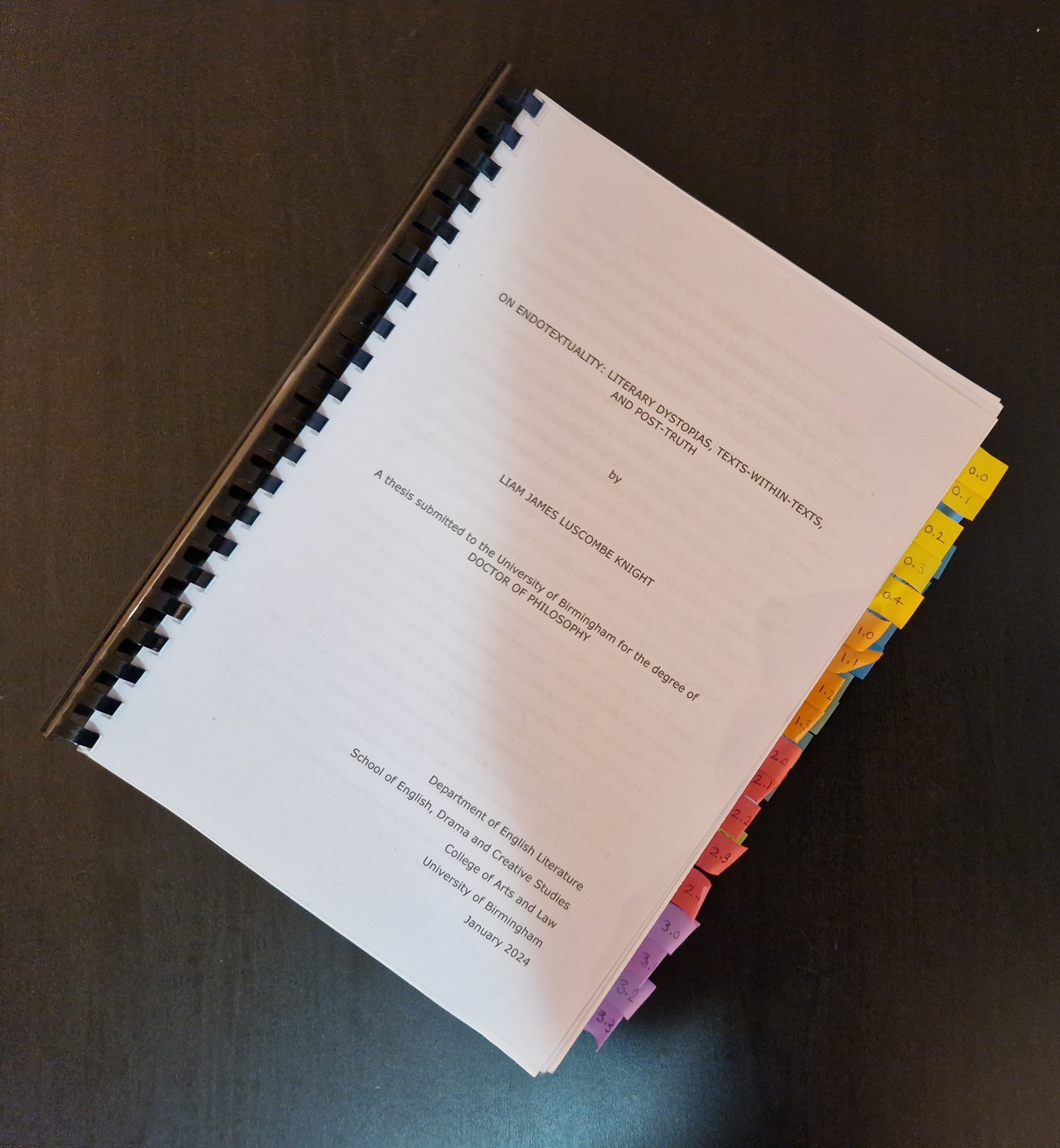 A spiral bound PhD thesis with the title "On endotextuality: literary dystopias, texts-within-texts, and post-truth" with many post-it note tabs sticking out along the right hand edge.